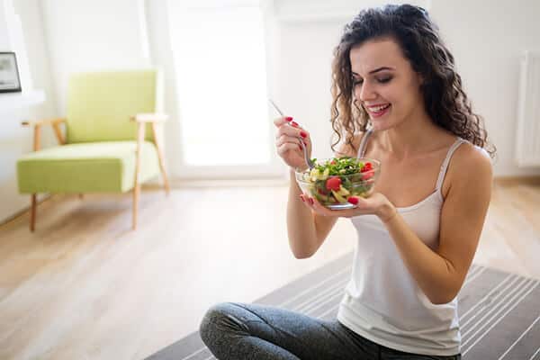 woman sitting on the floor on carpet eating a bowl of salad