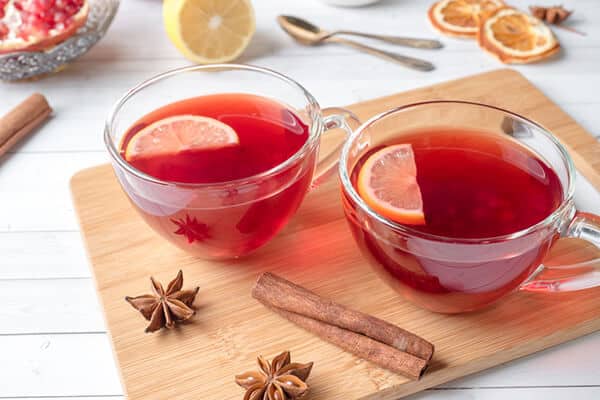 red tea with lemon slices on a wooden board next to cinnamon sticks