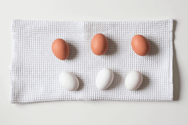 three brown eggs and three white eggs on a white cloth on a table