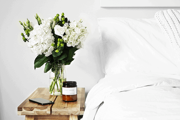 white bed with sheets, white flowers on a wooden bedside table