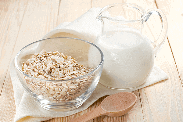oats in a glass bowl with wooden spoon next to bowl and a large glass jug of milk