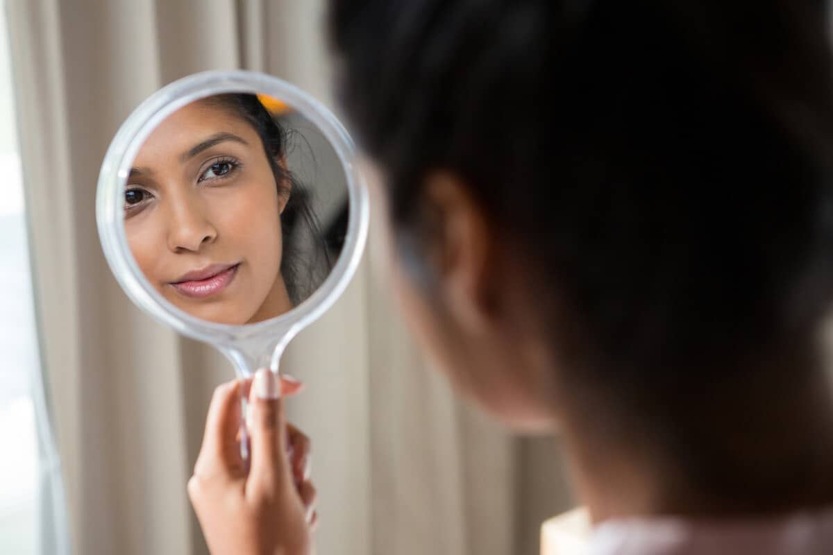 woman holding up a mirror and looking at herself in it
