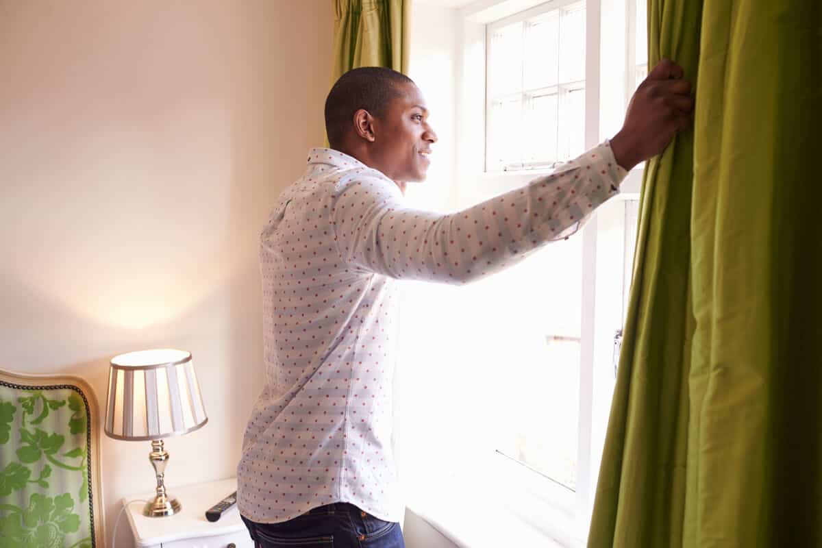 man opening window in bedroom and looking outside