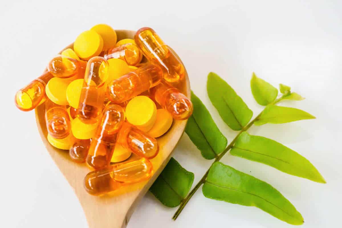 supplement pills in wooden sleep next to green plant leaf