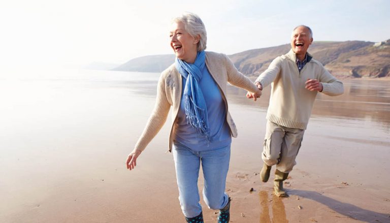 an elderly couple joyfully running along a beach while holding hands