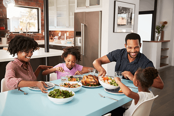 family of four sitting at dinner table and eating together