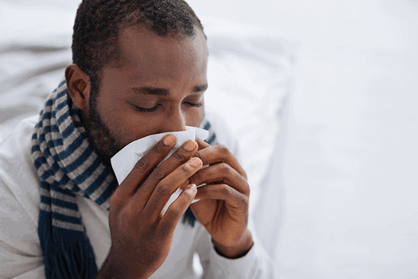 man with a scarf drinking a warm beverage from white mug sitting on bed